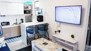 Un espace de vie compact comprenant un coin cuisine, un téléviseur à écran plat, une machine à café et une petite plante.