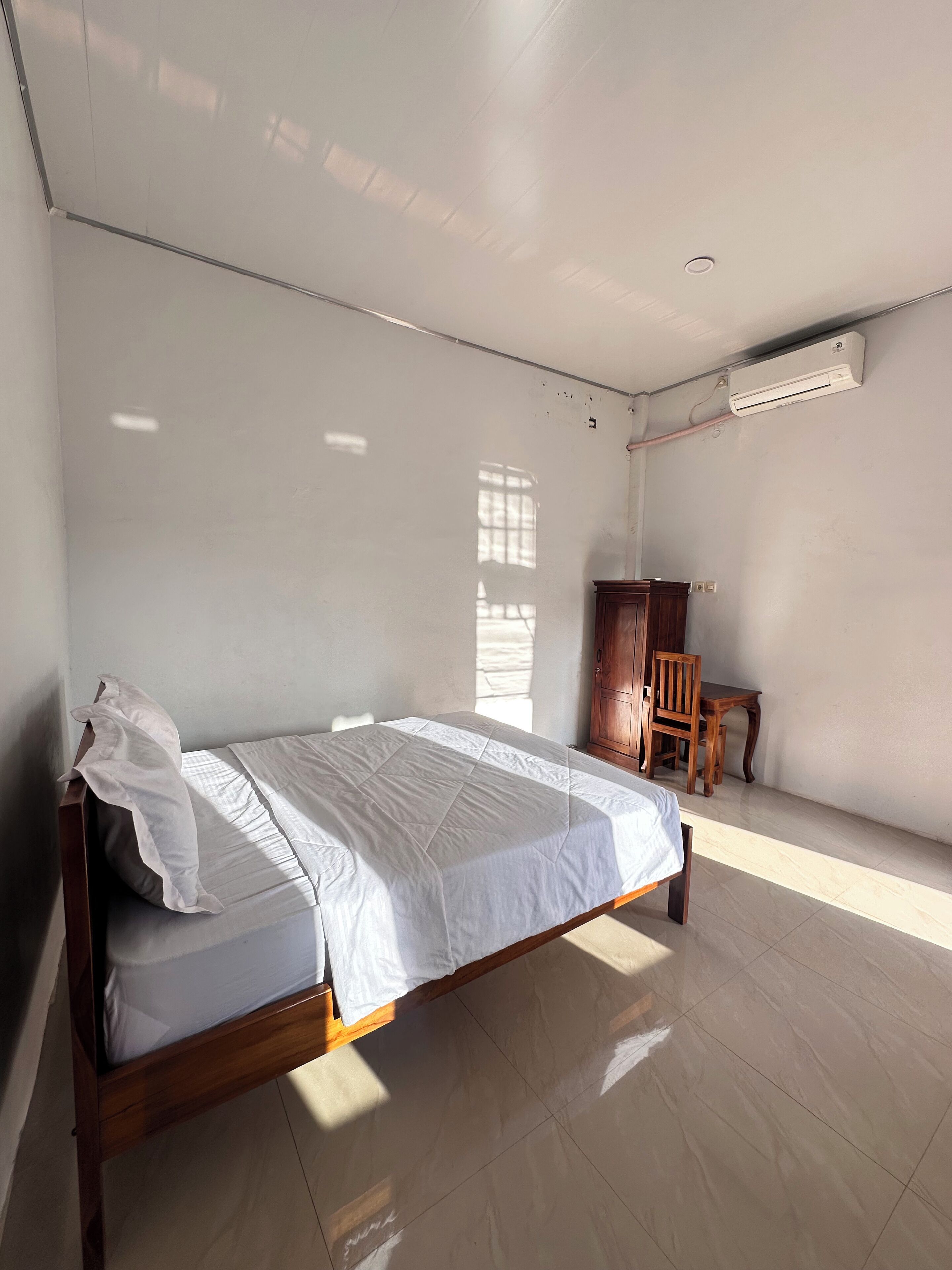 A bedroom with a bed, wooden furniture, and an air conditioning unit.