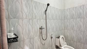 A bathroom with a toilet, a shower, and a hand soap dispenser on a shelf.