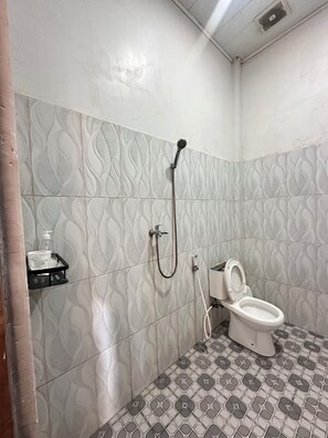 A bathroom with a toilet, a shower, and a hand soap dispenser on a shelf. - Charlitoz Homestay (Labuan Bajo)