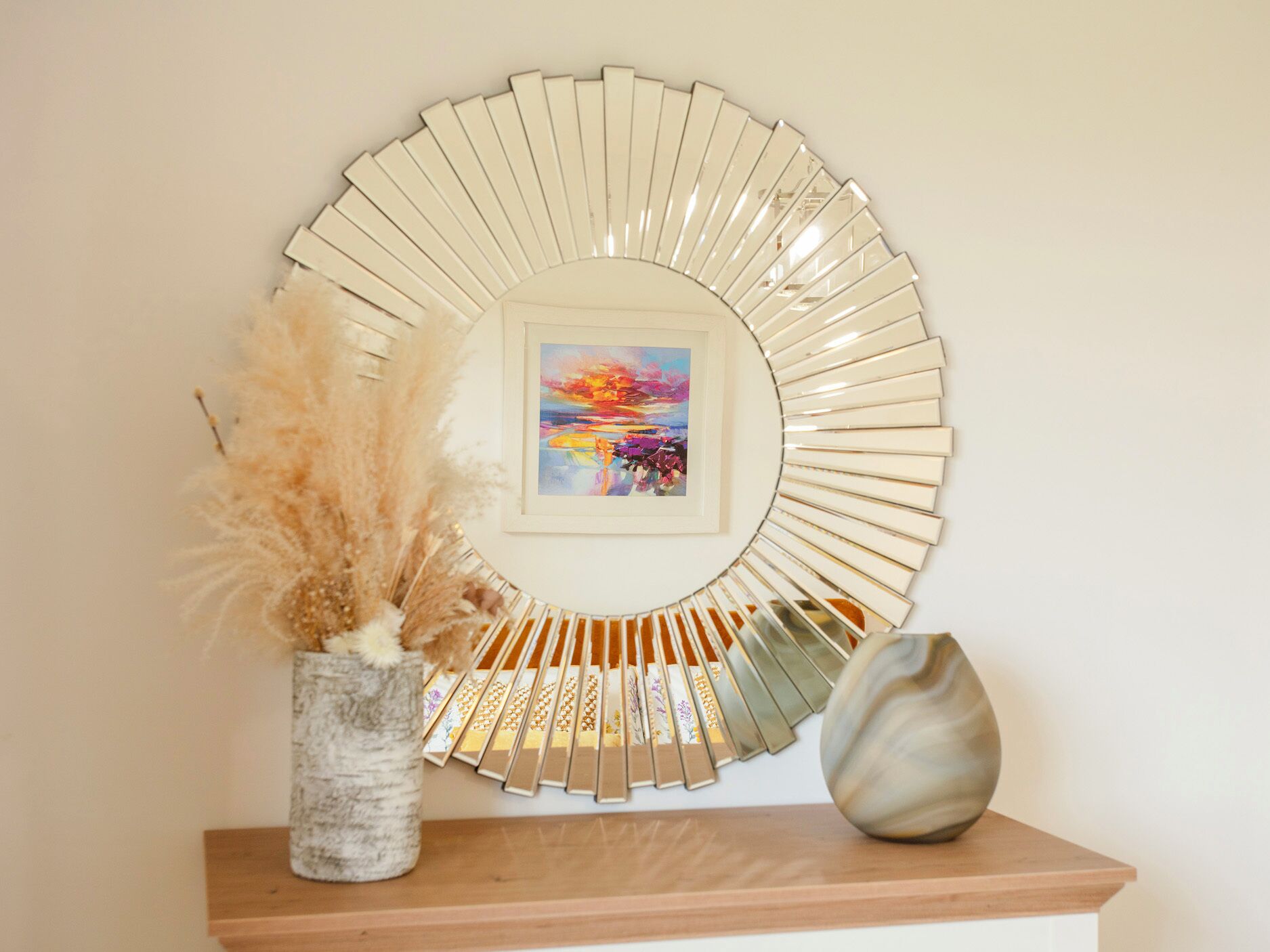 A circular wall decoration with a framed painting, a vase with dried plants, and a decorative object on a wooden shelf.