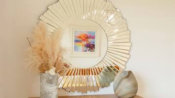 A circular wall decoration with a framed painting, a vase with dried plants, and a decorative object on a wooden shelf.