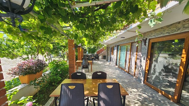 Un patio al aire libre con una mesa y sillas, rodeado de follaje y un muro de ladrillo.