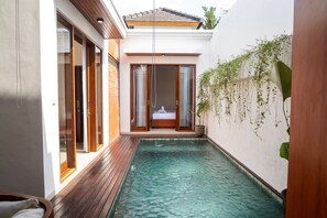 A modern pool area with a wooden deck, a bedroom with a bed and curtains, and a wall with hanging plants. - 2-bedroom villa in tranquil Bali (Bali)