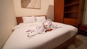 A neatly made bed with white linens, a heart-shaped towel arrangement, and rose petals on the bed.