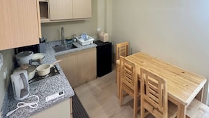 A compact kitchen with a granite countertop, wooden cabinets, a small refrigerator, and a dining table with chairs.