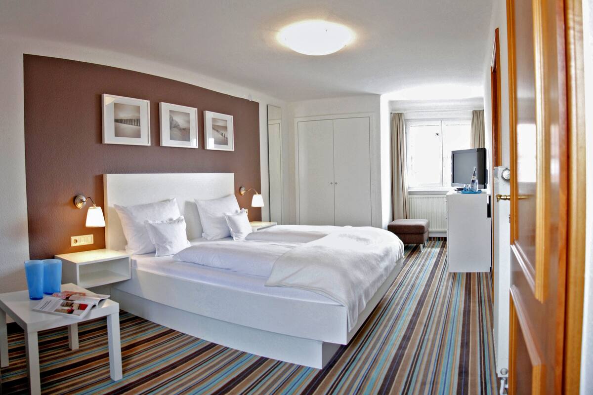 A hotel room with a bed, bedside tables, a desk, a television, and a wardrobe.