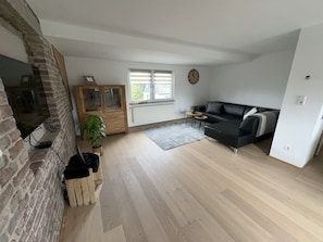 Una sala de estar con pared de ladrillo, mueble de madera, sofá negro y una pequeña mesa.