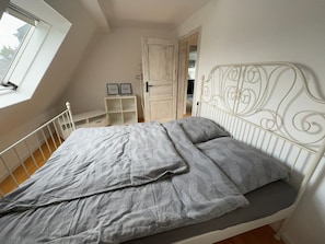 Un dormitorio con cama, ventana, puerta y cabecera de metal blanco.