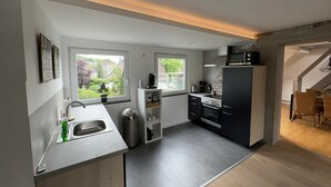 A modern kitchen with a built-in oven, a microwave, and a sink. There are windows providing natural light and a view of the outside. - Saarner Loft Apartment with Private Terrace, Garden, and Wi-Fi (Mülheim an der Ruhr)