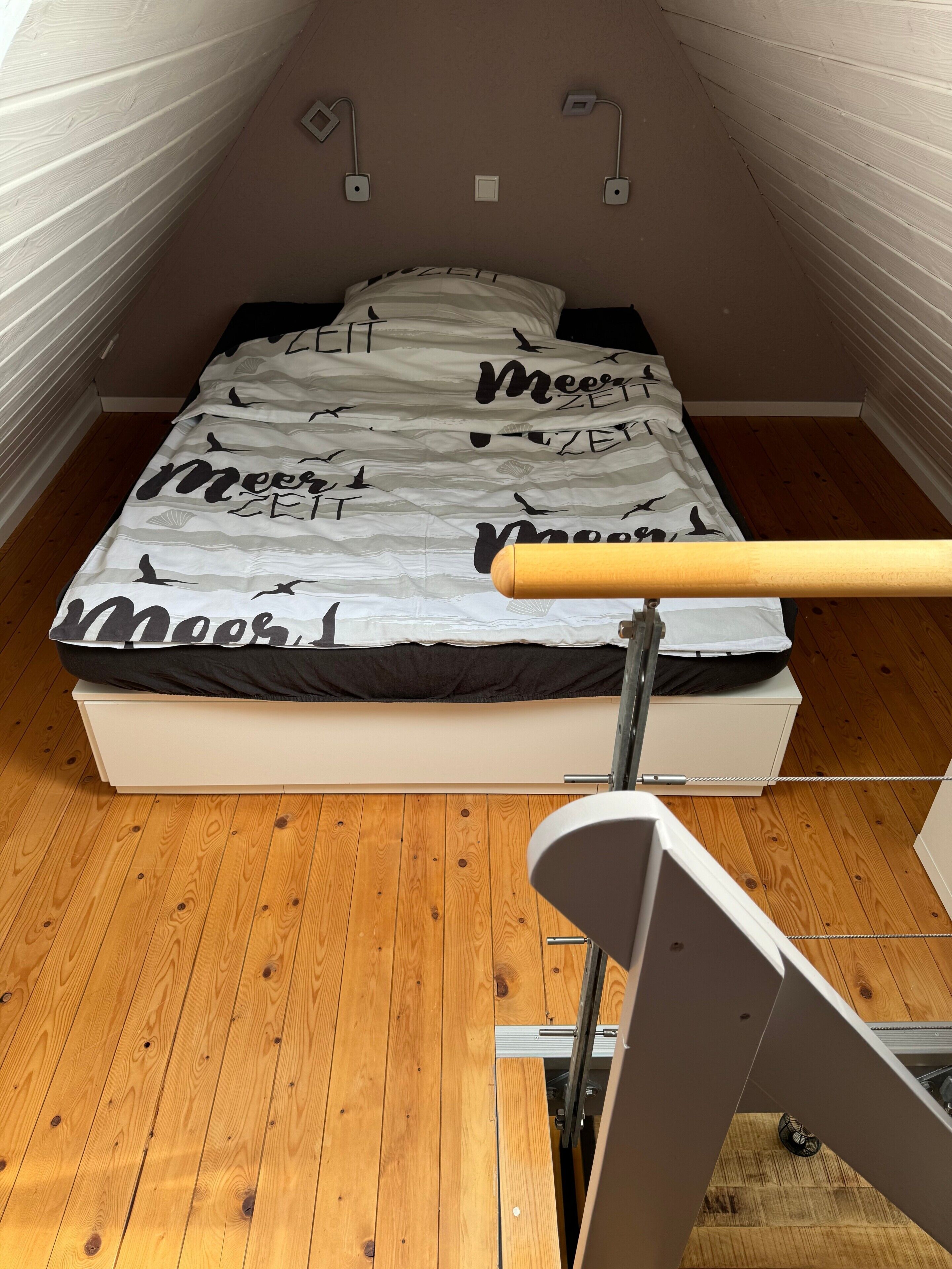 A bedroom with a bed, wooden flooring, and a sloped ceiling.