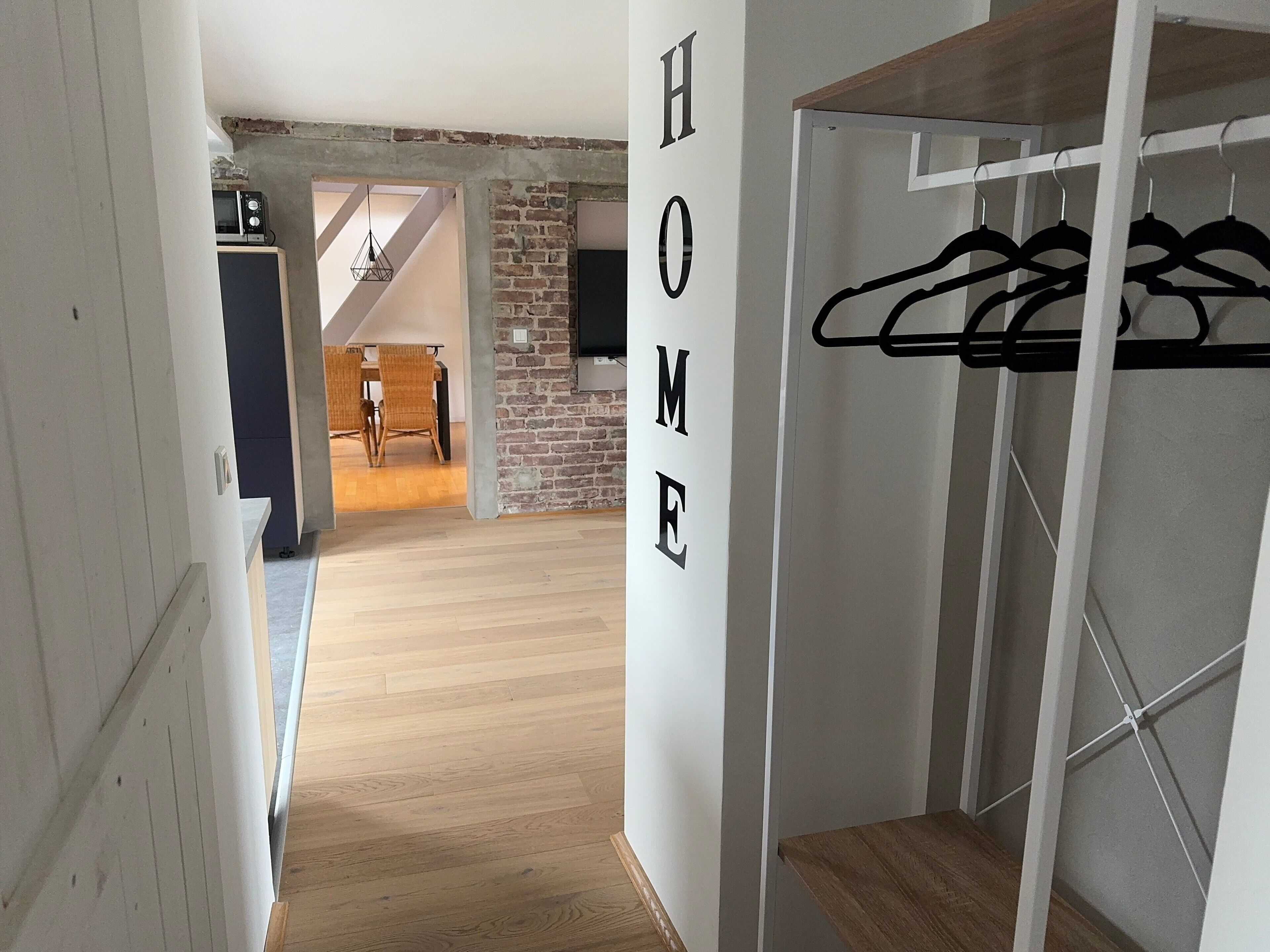 A hallway with a wooden floor, a coat rack, and a wall with the word 'HOME' spelled out.
