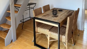 A modern interior with a staircase, dining table, wicker chairs, and a wall-mounted artwork. - Saarner Loft Apartment with Private Terrace, Garden, and Wi-Fi (Mülheim an der Ruhr)