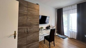 A modern living room with a wooden wardrobe, a flat-screen TV, a dining table with chairs, and a large window with curtains. - Riverside Retreat in Koblenz (Koblenz)