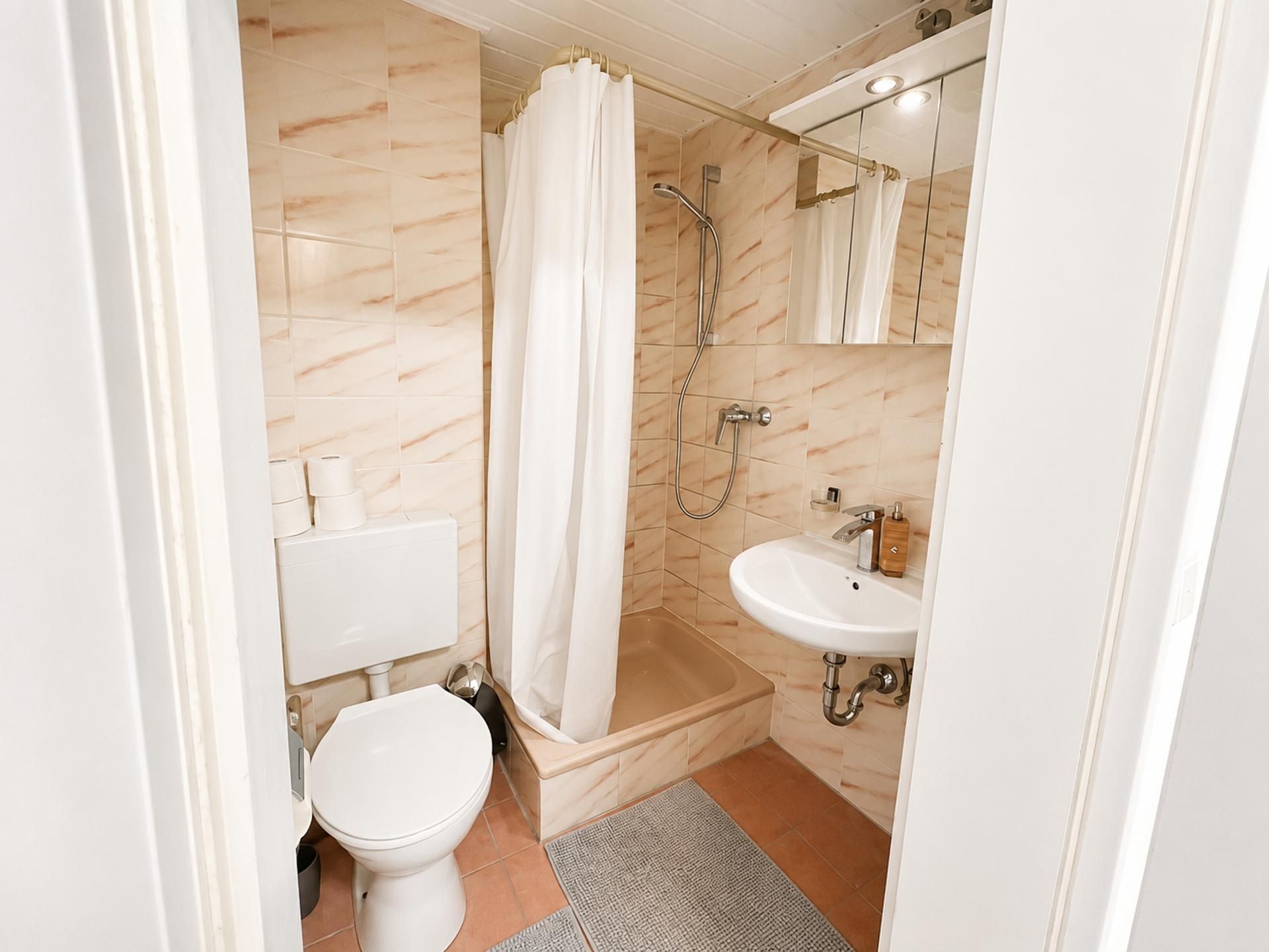 A bathroom with a toilet, a shower with a curtain, a sink, and a mirror.