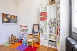 Une pièce comprenant une bibliothèque, un bureau, une chaise, un radiateur et une fenêtre.