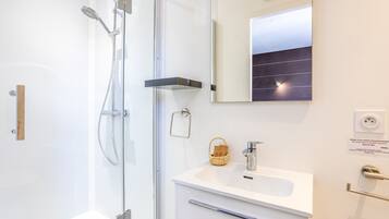 Un baño moderno con cabina de ducha de vidrio, un lavabo blanco, un espejo y un perchero para toallas.