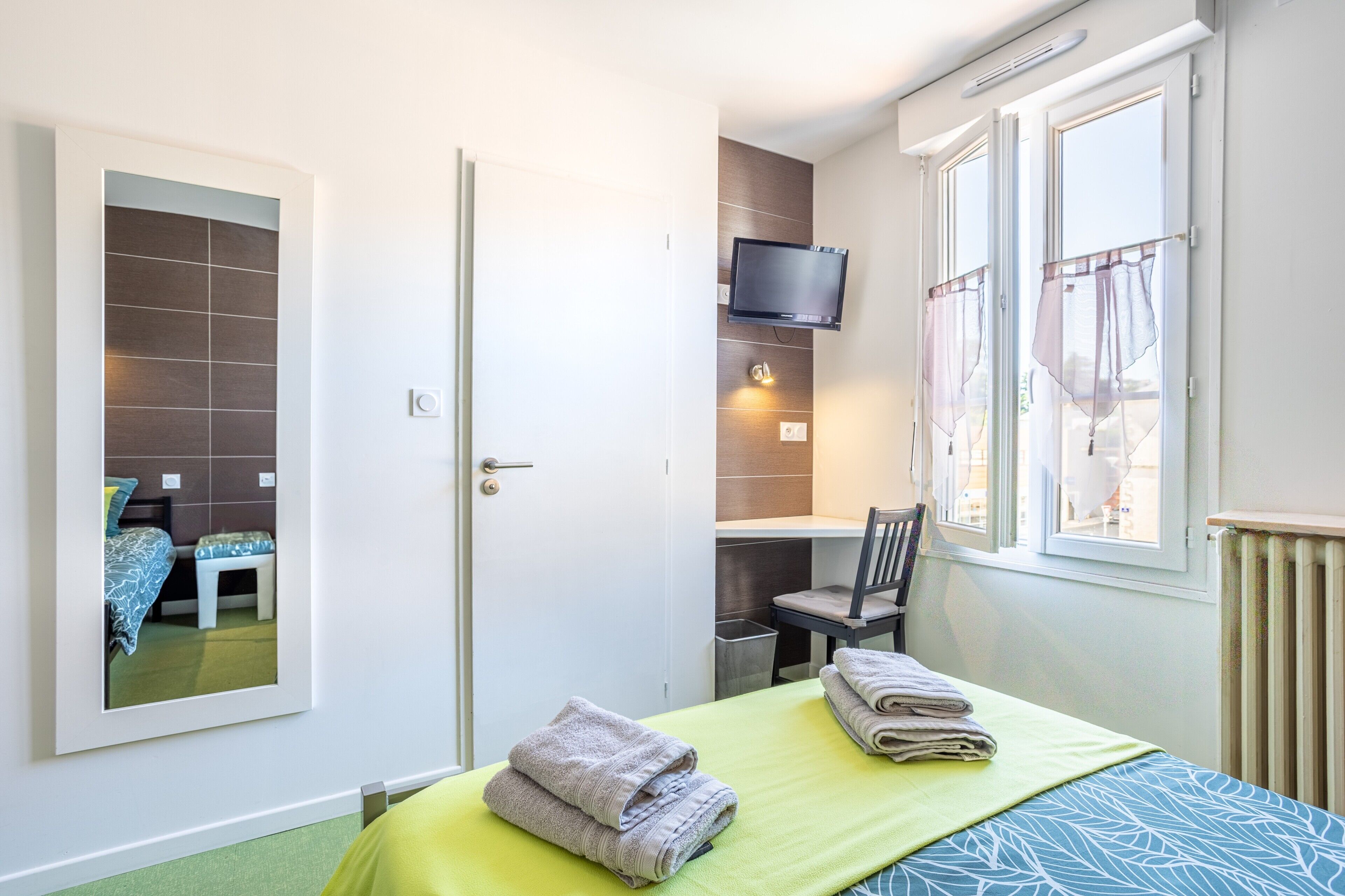 Une chambre d’hôtel avec un lit, un bureau, une chaise, une télévision et une fenêtre.