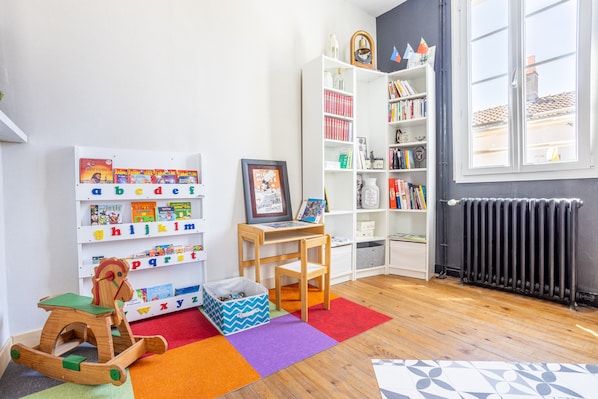 Une chambre d’enfant avec une bibliothèque, un cheval à bascule, un tableau encadré et un radiateur.