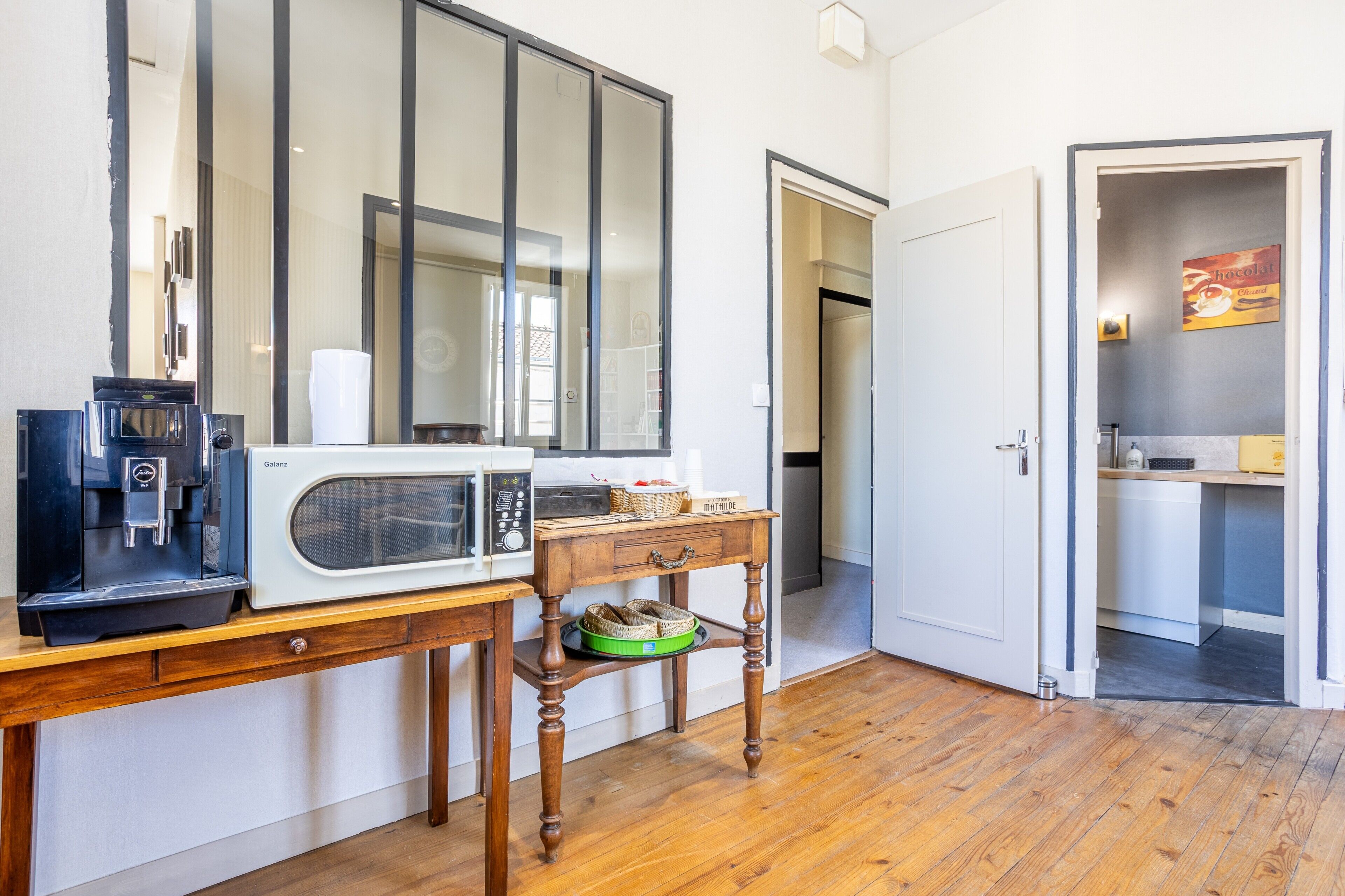 A kitchenette with a coffee machine, microwave, and a small table with a basket.