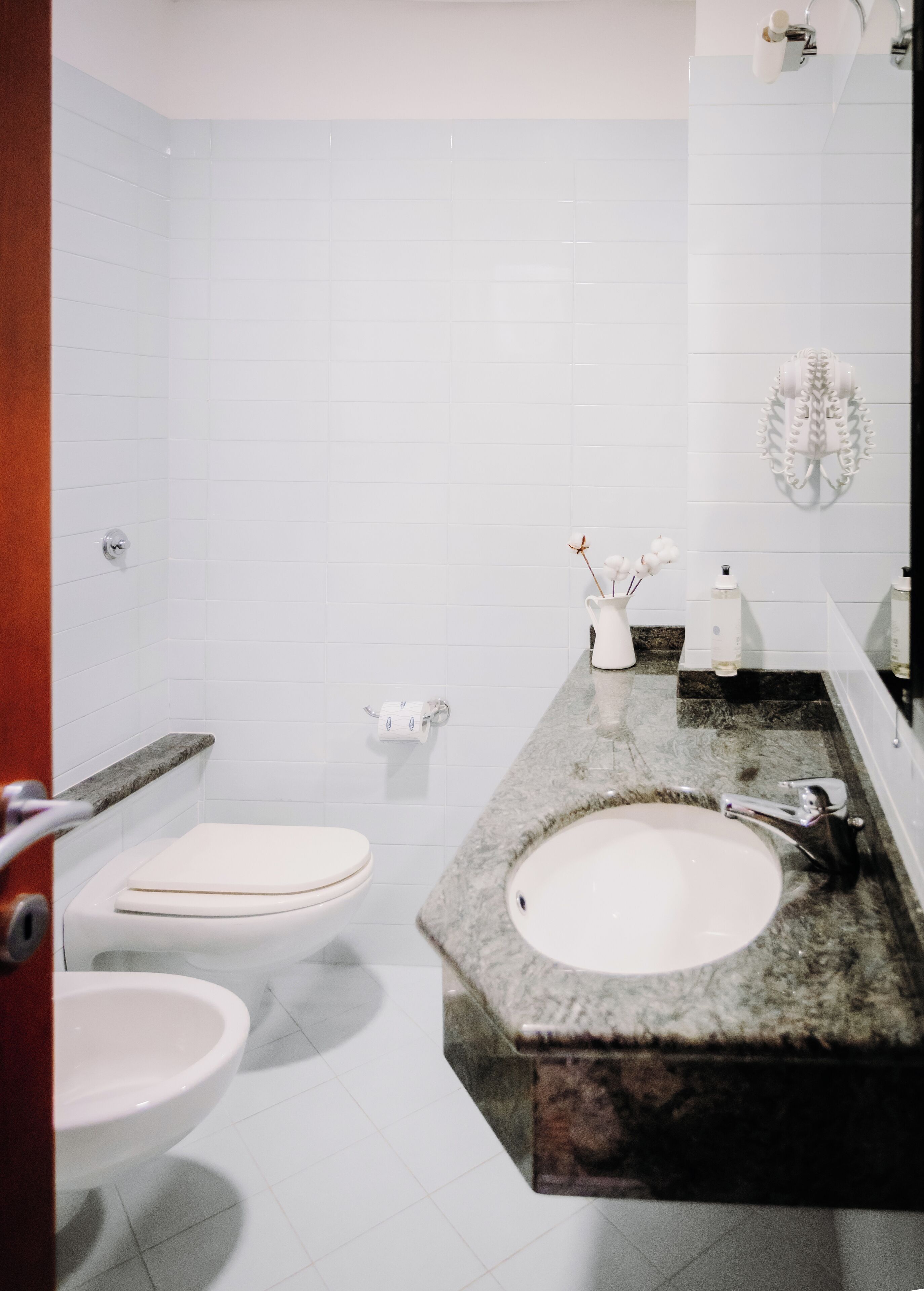 A bathroom with white tiled walls, a marble sink, and a toilet.
