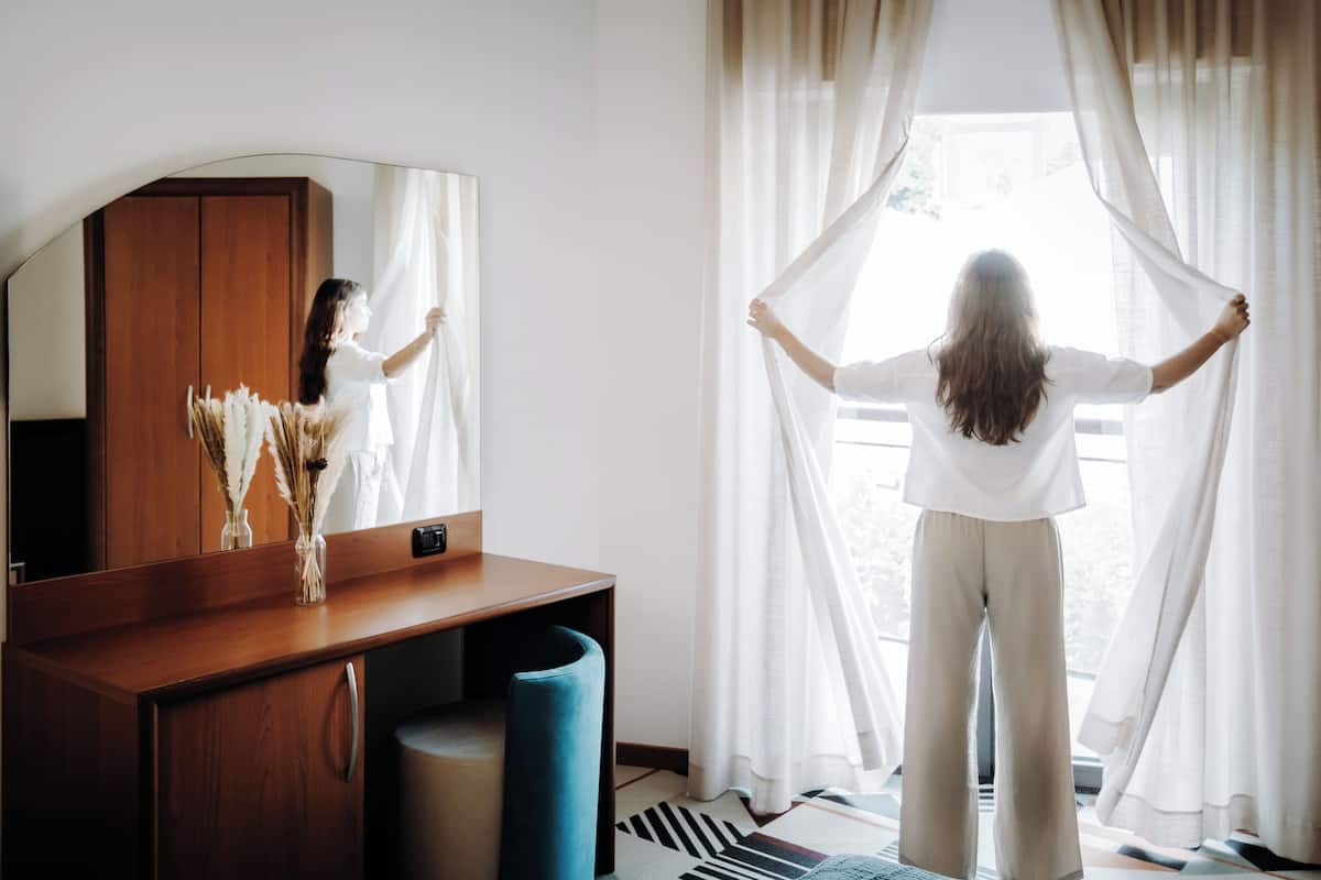 A room with a wooden desk, a mirror, and a window with sheer curtains.