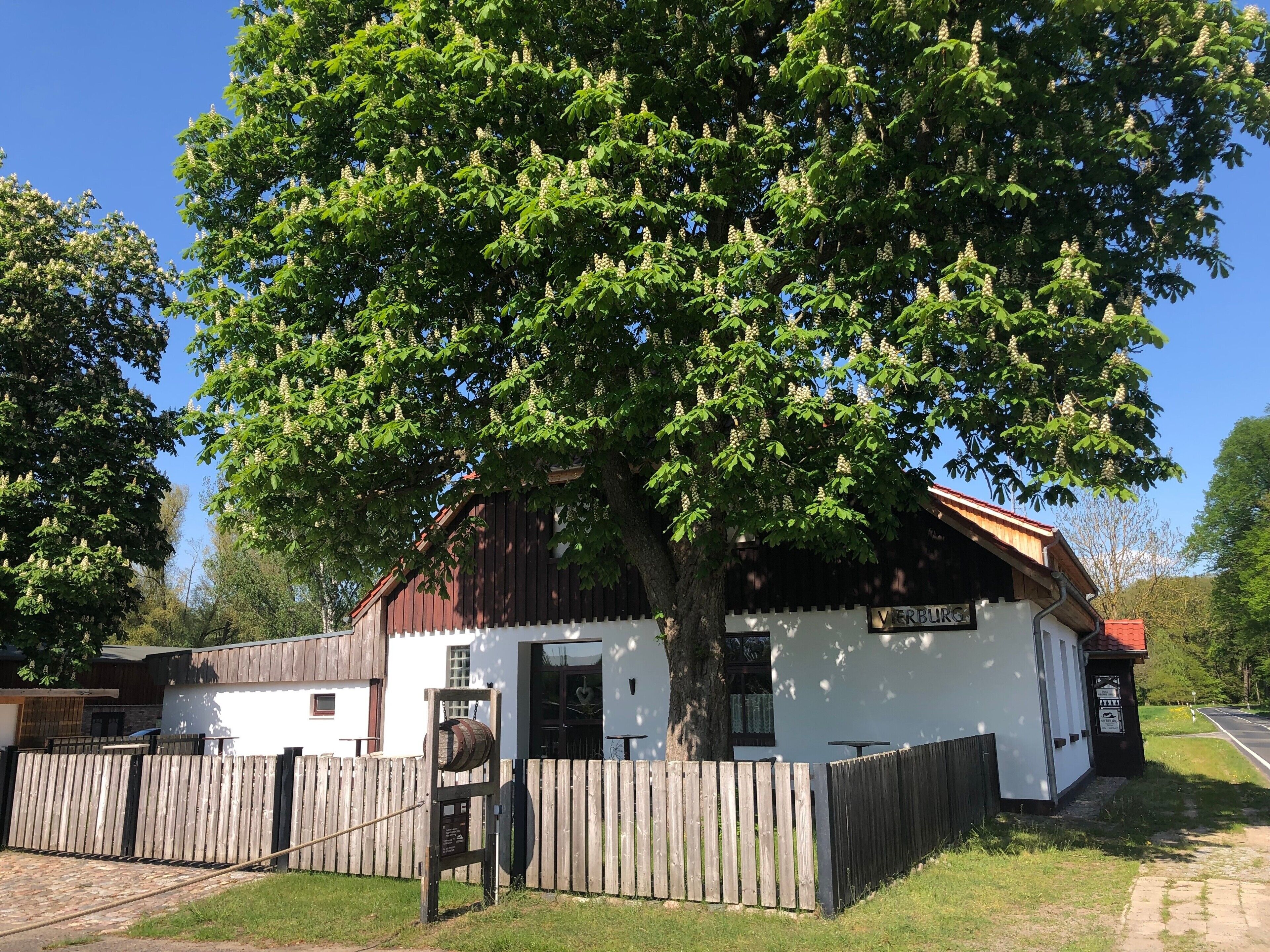 Un edificio blanco con valla de madera, un árbol en primer plano y un cartel que dice 'VIBUR'.