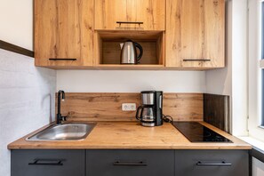 A kitchen with wooden cabinets, a stainless steel sink, a coffee maker, and an induction cooktop. - Cozy 1-Room Apartment with Shared Terrace, Garden & Wi-Fi (Bützow)