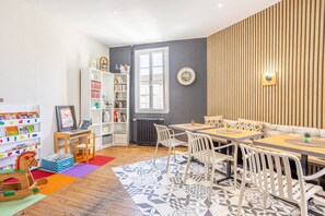 A room with a wooden dining table, white chairs, a bookshelf, and a radiator. - Room 'N°01' with Wi-Fi (Chantonnay)