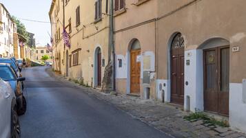 Une rue étroite bordée de bâtiments historiques, dont certains présentent des portes et des fenêtres en arc de cercle, et où quelques voitures sont garées le long du trottoir.