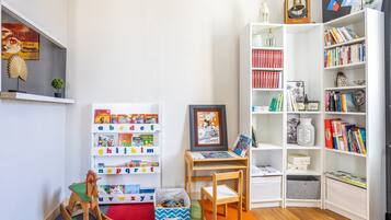 Espaço infantil com prateleiras do alfabeto, uma pequena mesa com porta-retrato e estante cheia de livros.