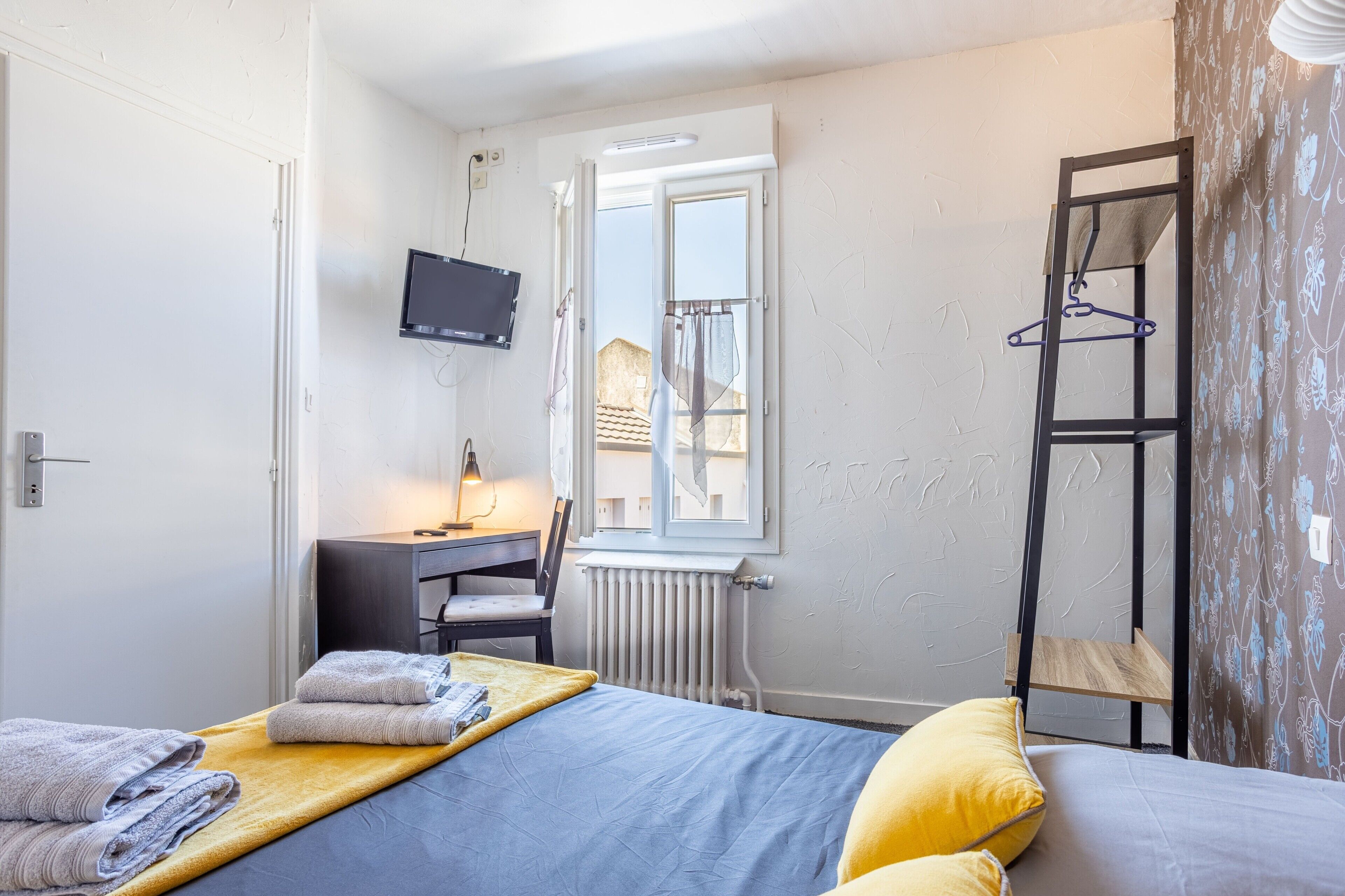 Une chambre à coucher comprenant un lit, un bureau, une chaise, un radiateur, une télévision et une fenêtre donnant sur un paysage agréable.