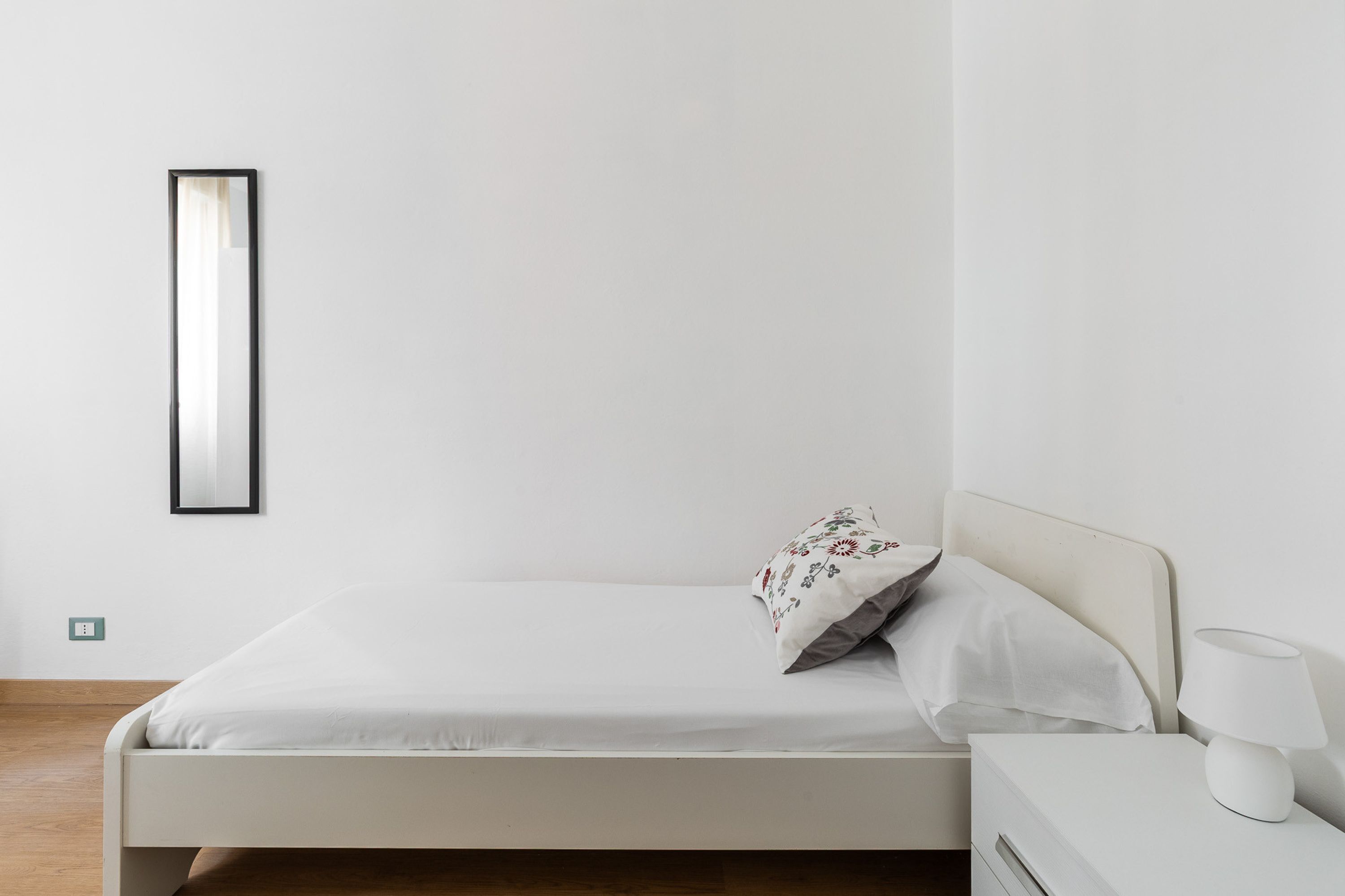 Une chambre à coucher minimaliste avec un lit simple, une table de chevet avec une lampe et un miroir fixé au mur.