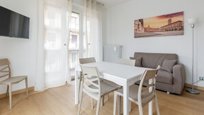 A modern living room with a white dining table, beige chairs, a grey sofa, and a painting of a cityscape on the wall. - Bologna City Center View by Wonderful Italy (Bologna)