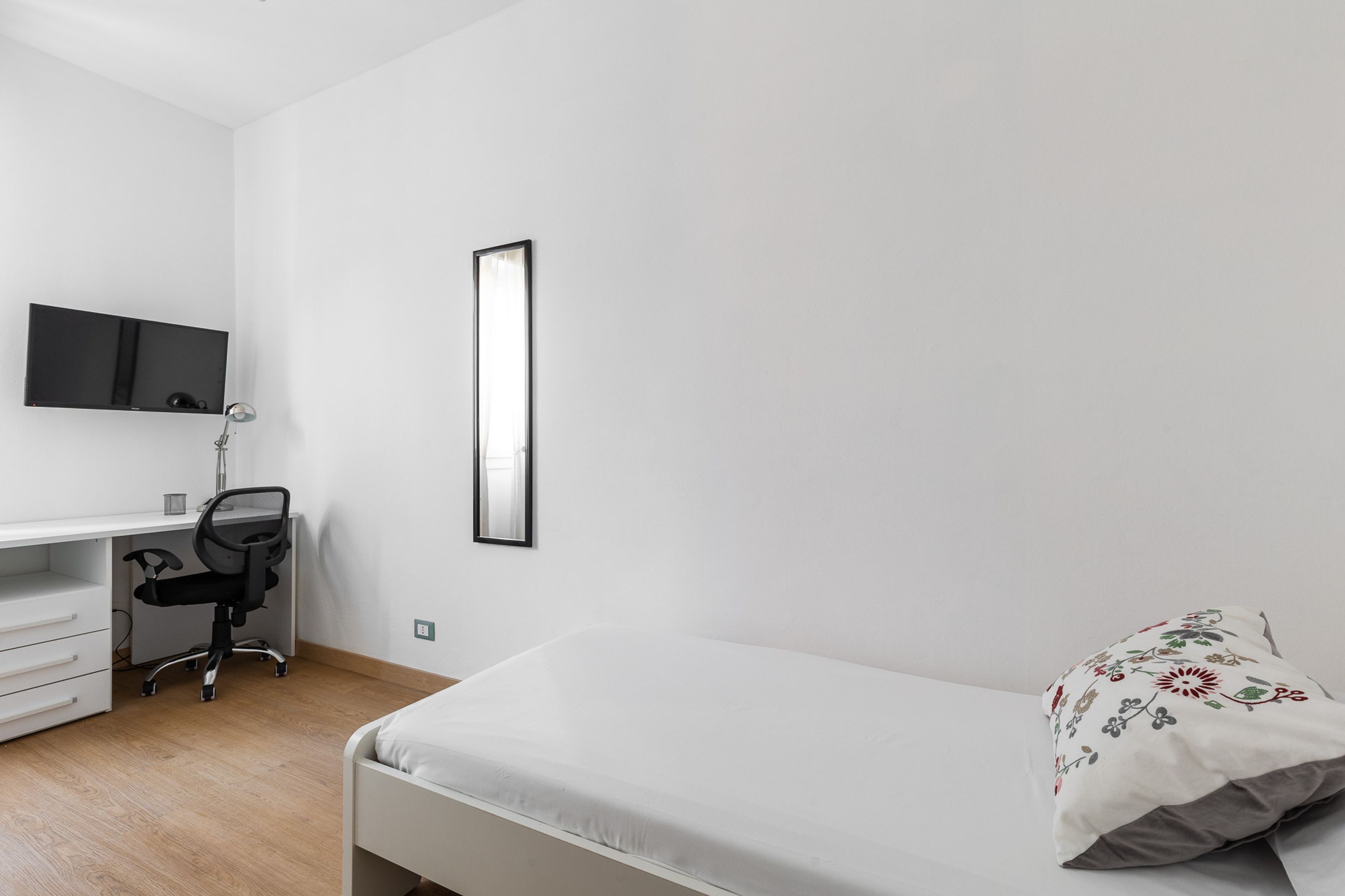 Une chambre à coucher comprenant un lit, un bureau avec une chaise, un téléviseur fixé au mur et une table de chevet.