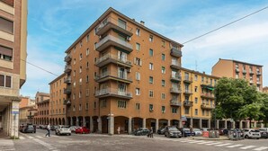 A multi-story residential building with balconies, a crosswalk, and parked cars. - Bologna City Center View by Wonderful Italy (Bologna)