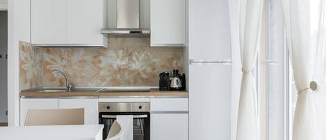 Una cuina moderna amb armaris blancs, una campana extractora d'acer inoxidable, forn integrat i cafetera al taulell.