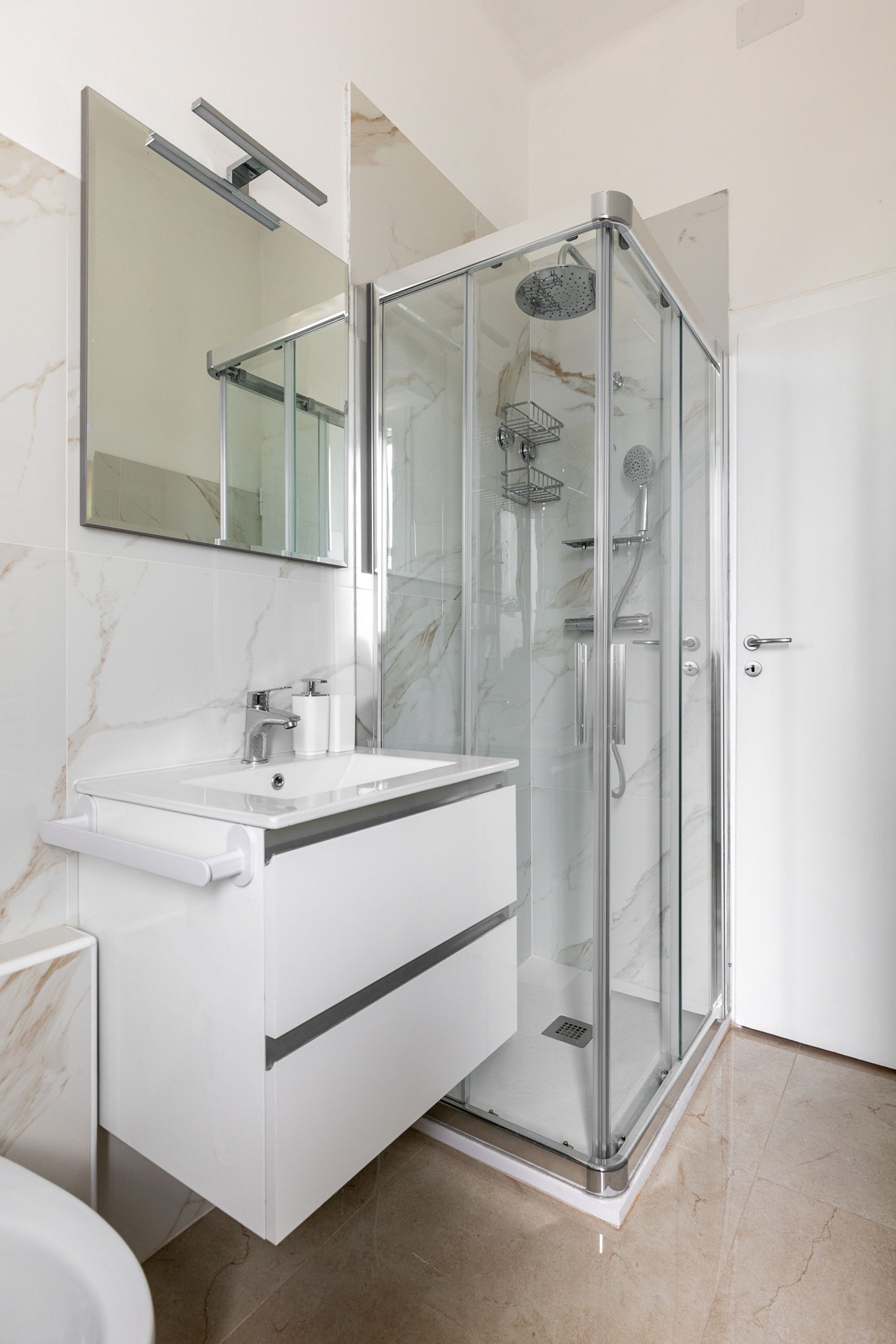 Een moderne badkamer met een douchecabine van glas, een wit wastafelmeubel met spiegel en marmeren wanden.