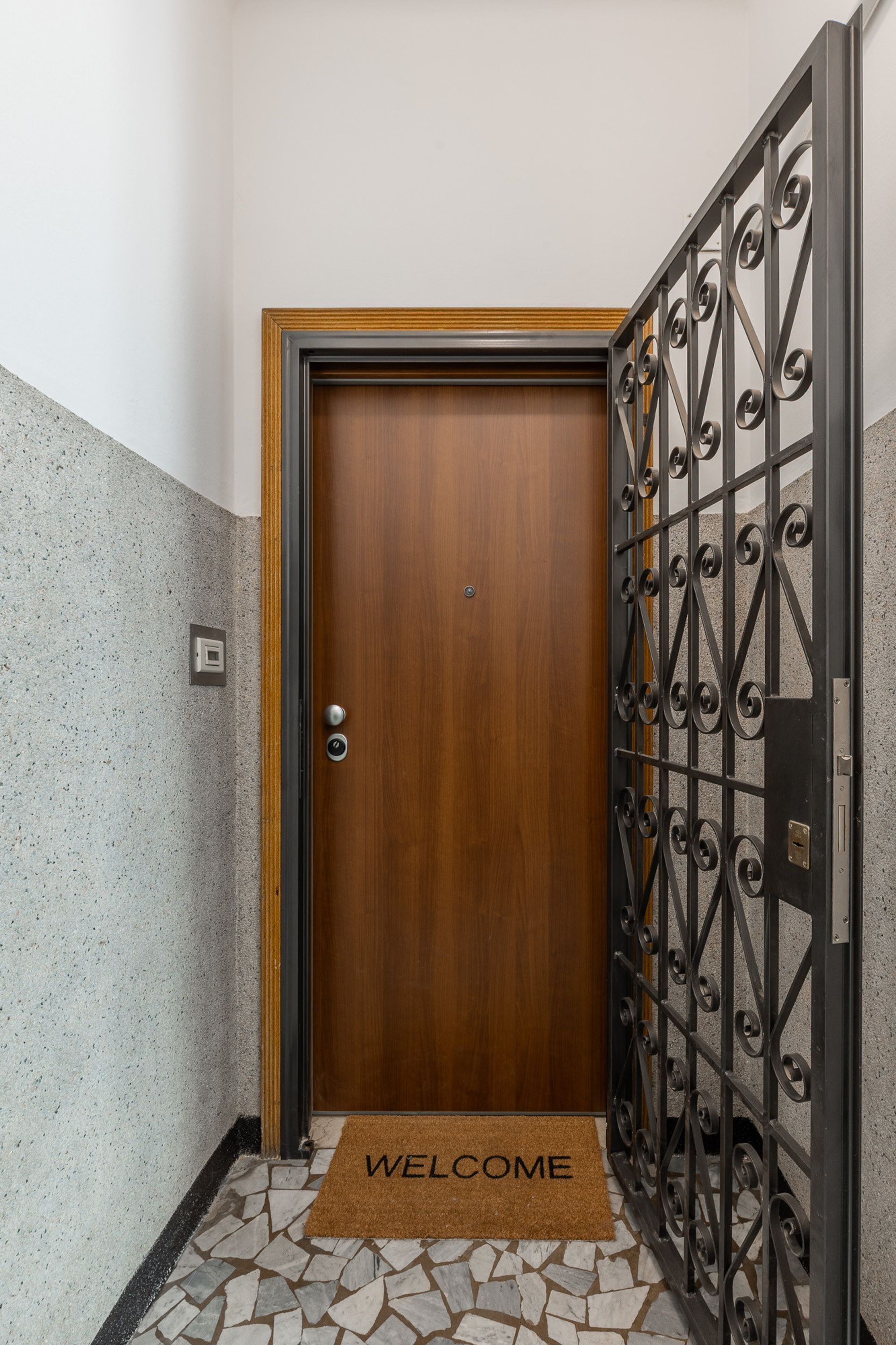Une porte en bois avec un portail en métal, un paillasson et un mur à texture.
