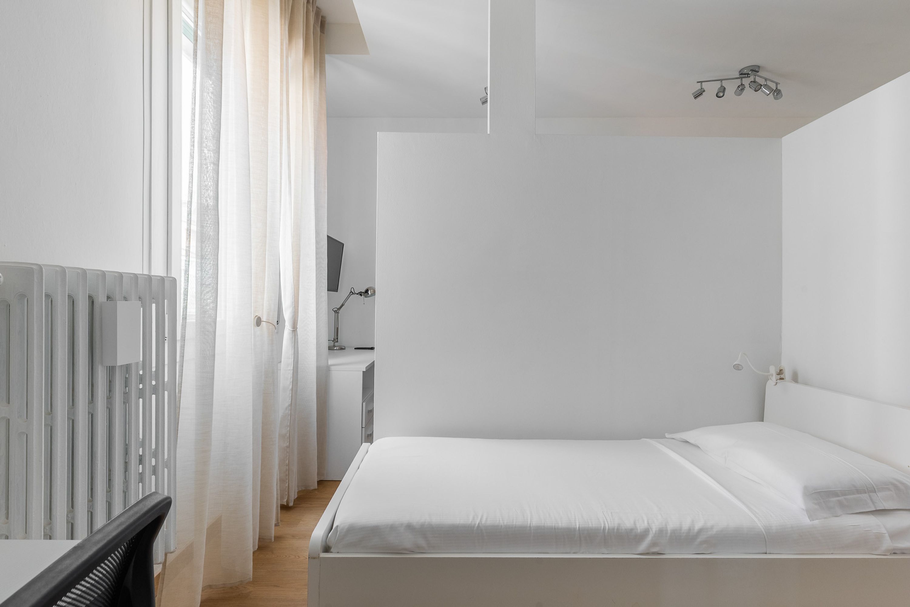 A minimalist bedroom with a bed, a desk, and a chair.