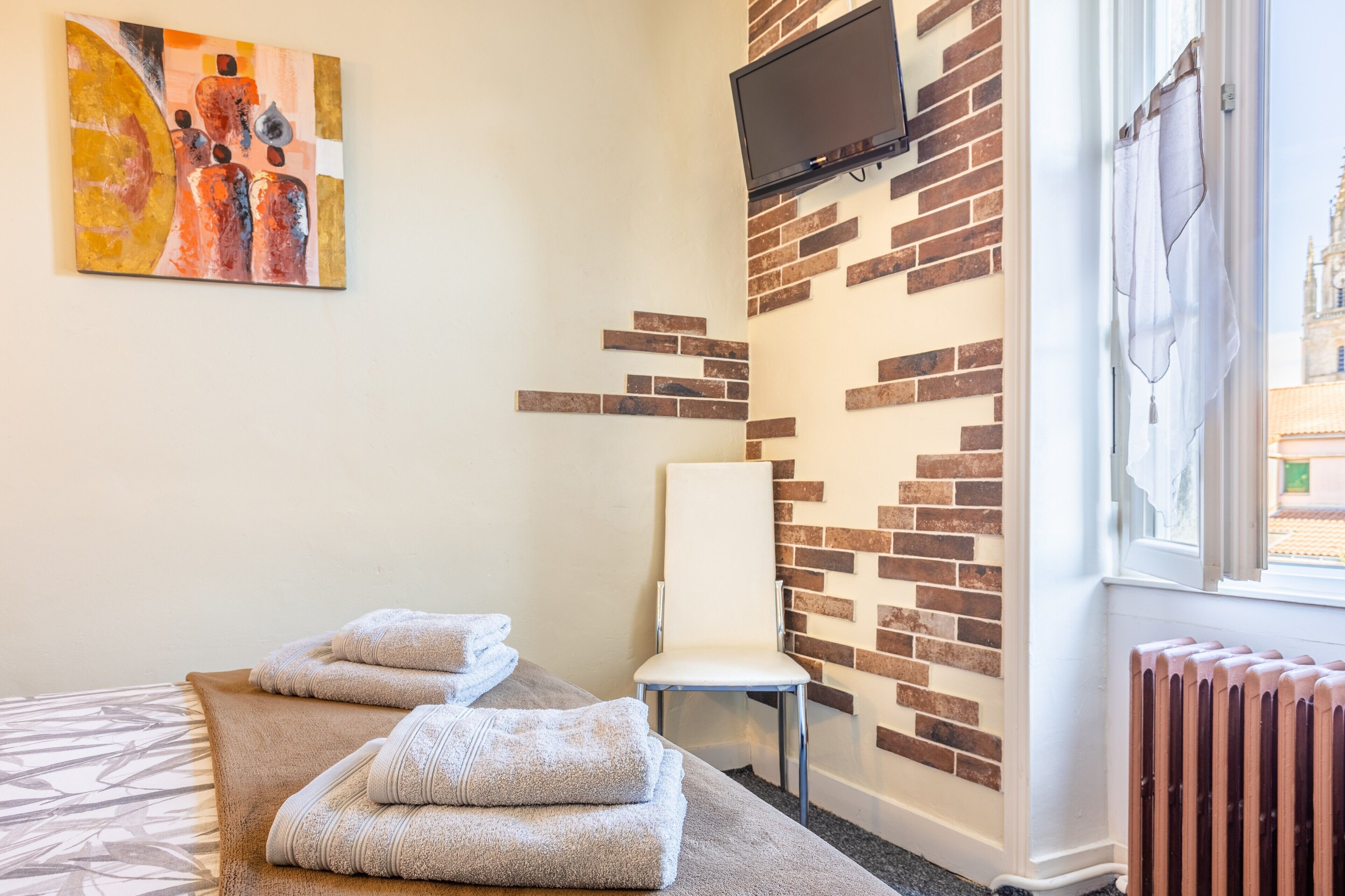 Ein Zimmer mit einer Massageliege, Handtüchern, einem Sessel, einem Fernseher und einer Ziegelwand.
