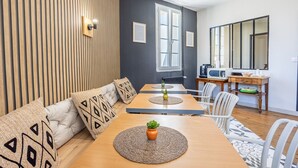 A modern living room with a sofa, dining table, and chairs. There is a kitchen area with a microwave and a refrigerator. - Standard Room 'N°11' with Wi-Fi (Chantonnay)