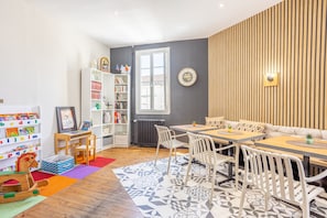 Una habitación con una mesa de comedor de madera, sillas blancas, una estantería y un radiador.