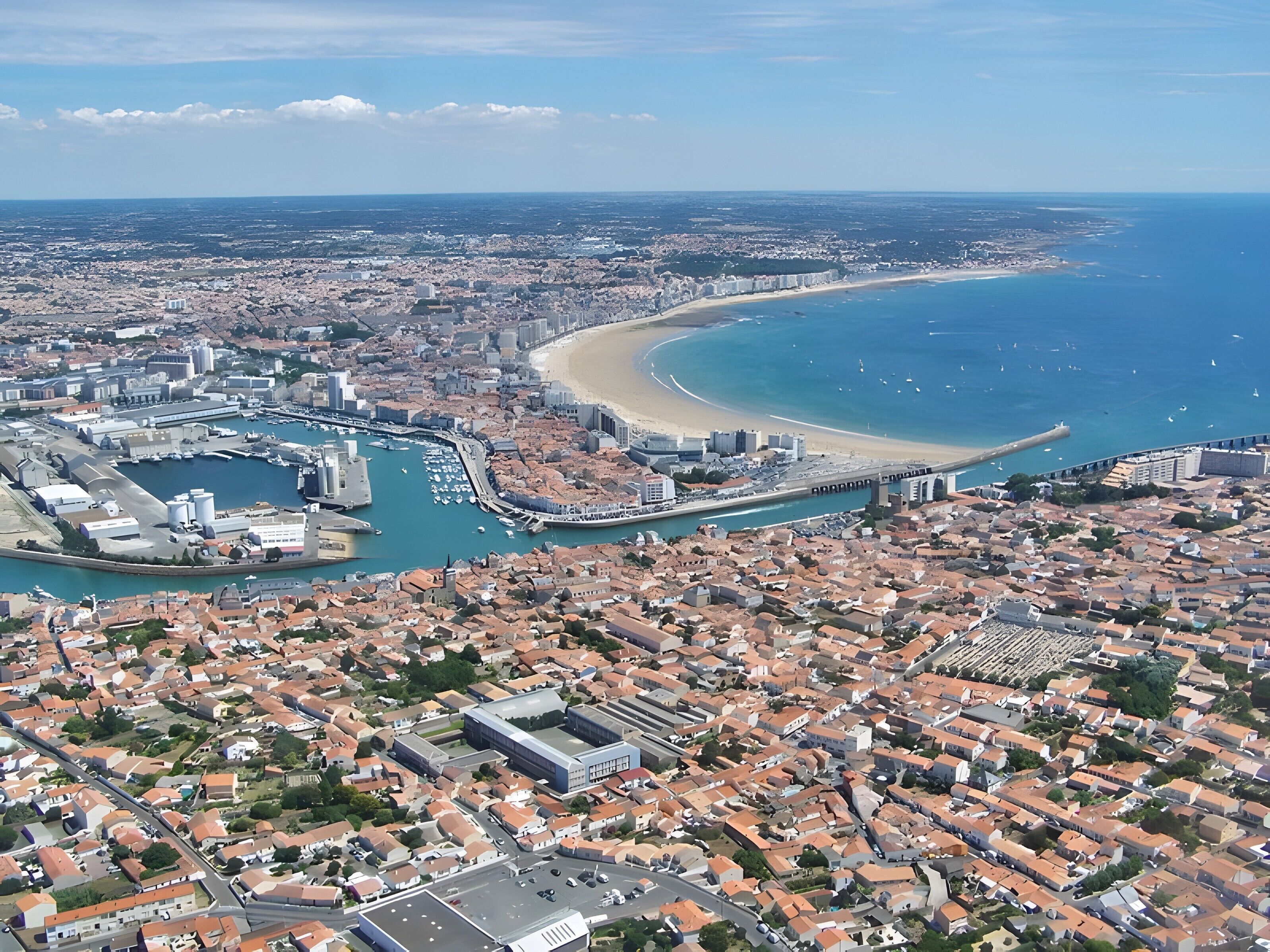 Vue aérienne d’une ville côtière avec un port de plaisance, une plage et des quartiers résidentiels urbains densément peuplés.
