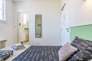 Une chambre à coucher avec un lit, un miroir, un radiateur, une porte et une fenêtre.