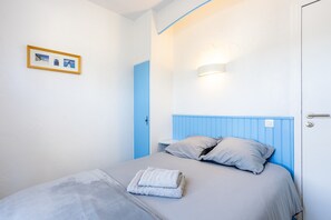Un letto rifatto con cuscini, un asciugamano piegato e una cornice con una foto appesa al muro.