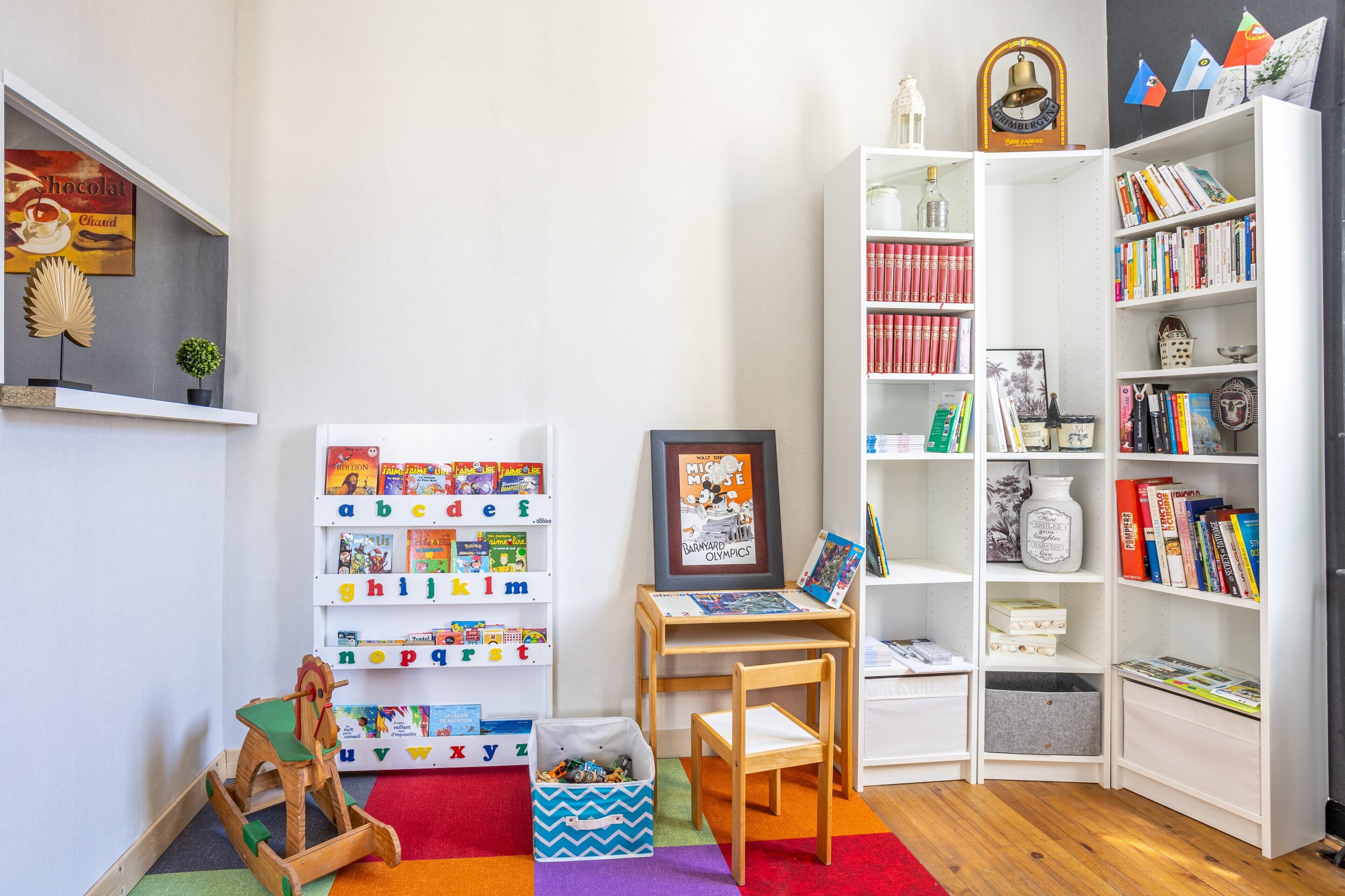 Espaço infantil com prateleiras do alfabeto, uma pequena mesa com porta-retrato e estante cheia de livros.