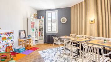 Een kamer met een houten eettafel, witte stoelen, een boekenkast en een radiator.