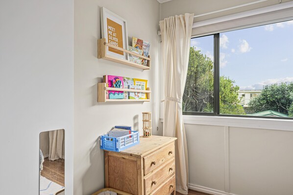 A room with a wooden dresser, a window with curtains, and shelves with books and decorative items.
