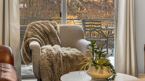 A cozy living room with a plush armchair, a round table with a plant, and a view of a balcony with chairs and a table. - Right on the River! Mtn Cabin w/ Deck & Fireplace (Shawnee)